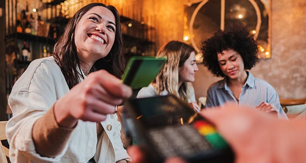 A group of girl friends get dinner together. The woman in the foreground is paying with her card using tap to pay. A group of girl friends get dinner together. The woman in the foreground is paying with her card using tap to pay.