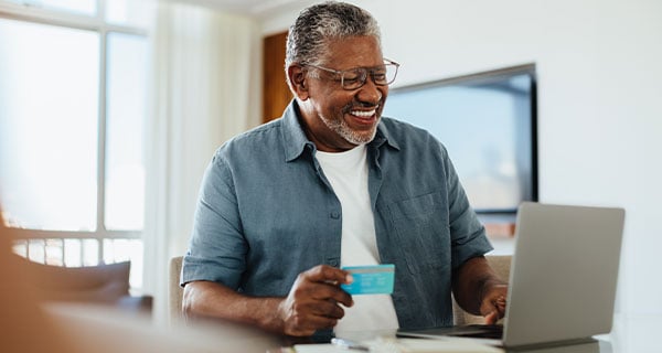 A man smiling while paying for something online using his credit card.  A man smiling while paying for something online using his credit card.